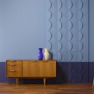 A vintage sideboard with a 3D wall panel featuring a repeating circular pattern in a room with blue walls and a wooden floor.