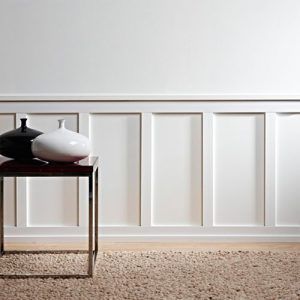 White wall with elegant wall paneling, brown rug and art deco table with black and white vases. 