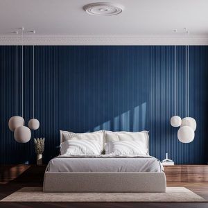 A bedroom with a blue accent wall featuring 3D wall panels, a large bed with white bedding, and a cluster of hanging pendant lights.
